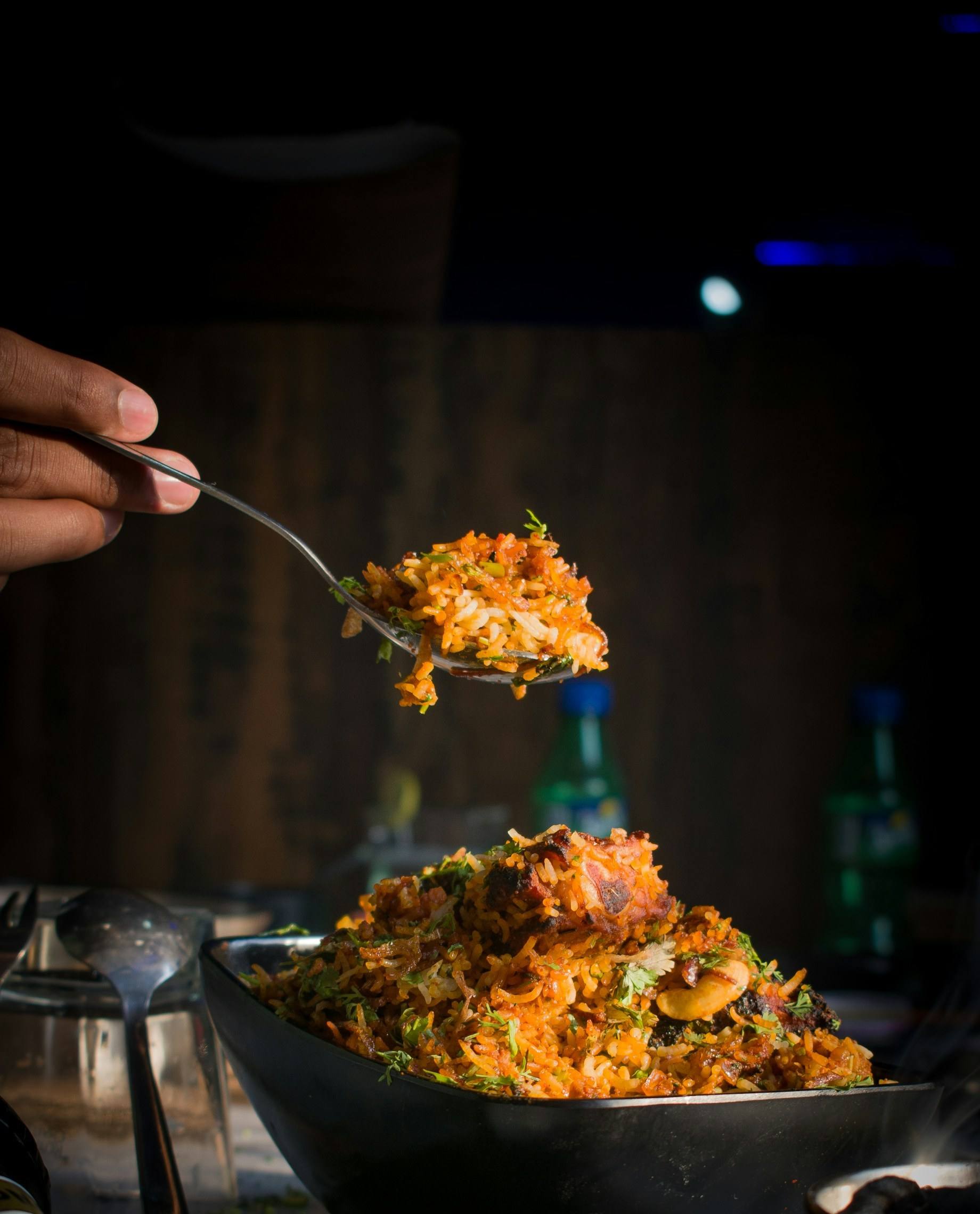 Biriyani lifted from the pot on a spoon, in low warm light