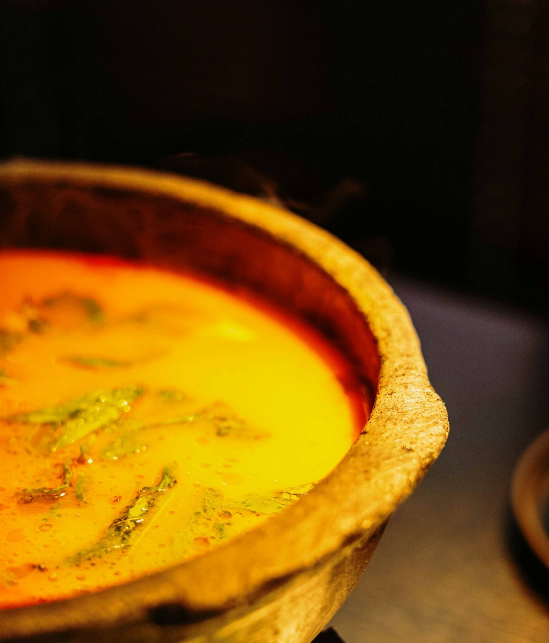 A golden curry in a rustic clay pot, glowing in low light