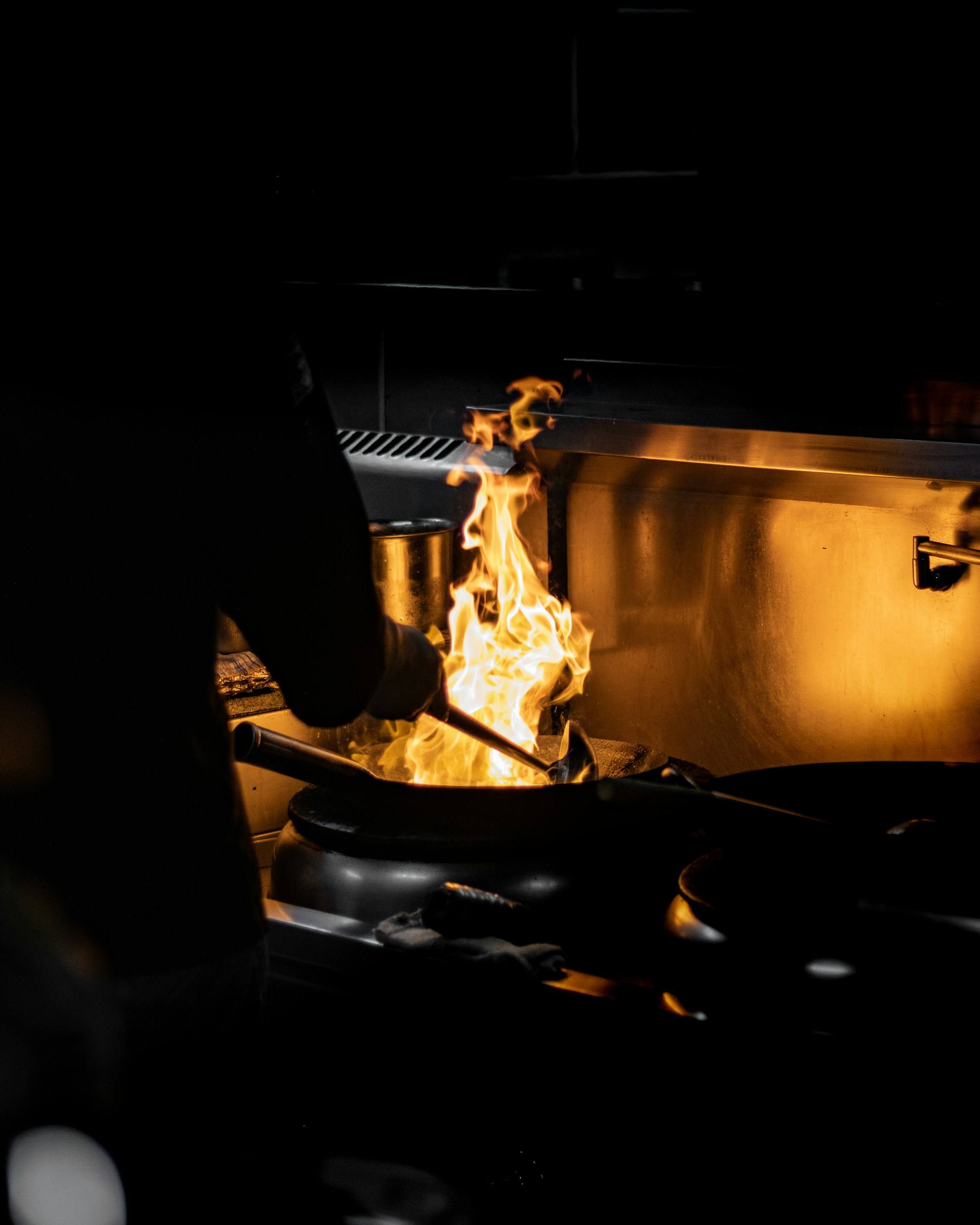Flames rising from a pan in a dark kitchen